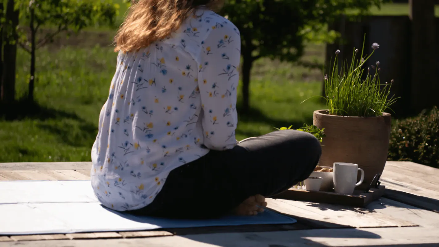 Eine Frau sitzt auf einer Kühlmatte auf einer Holzterrasse im Garten.